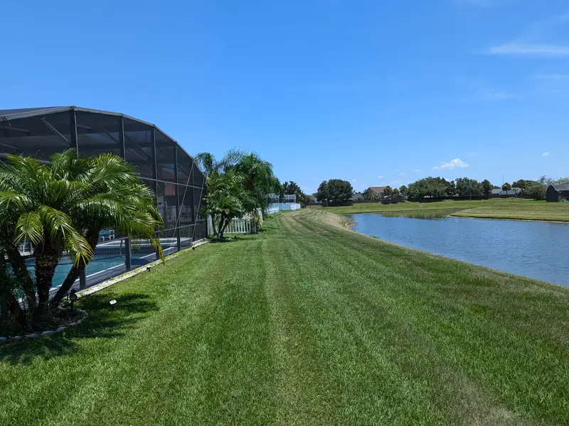 Striped back lawn running down to the lake behind a screened pool enclosure